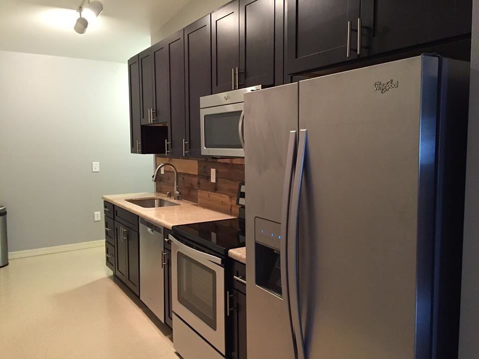 Inspiration for a transitional laminate floor kitchen remodel with an undermount sink, shaker cabinets, black cabinets, granite countertops, brown backsplash, wood backsplash and stainless steel appliances