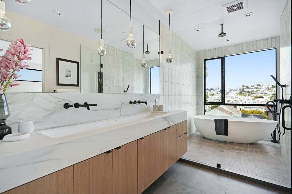 Photo of a large contemporary master wet room bathroom in San Francisco with flat-panel cabinets, medium wood cabinets, a freestanding tub, white tile, white walls, ceramic floors, a trough sink, marble benchtops, an open shower and white benchtops.