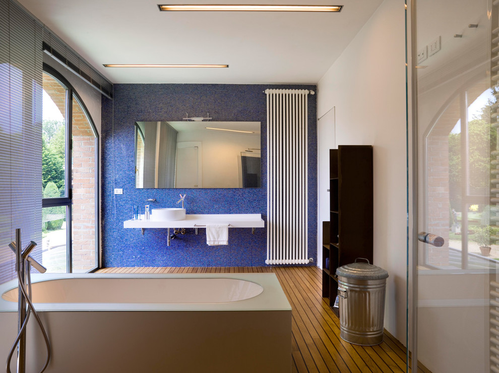 This is an example of a large contemporary bathroom in Florence with a freestanding tub, blue tile, white walls, a vessel sink and medium hardwood floors.