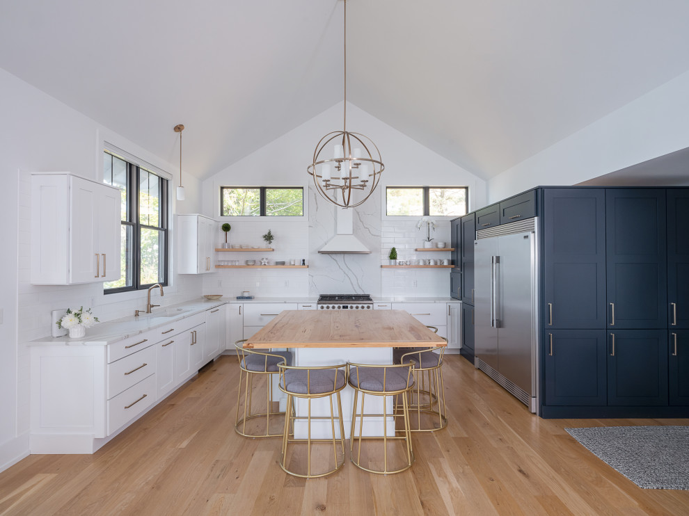 This is an example of a modern eat-in kitchen in New York with an undermount sink, flat-panel cabinets, blue cabinets, wood benchtops, white splashback, marble splashback, stainless steel appliances, light hardwood floors, with island, brown floor, brown benchtop and vaulted.