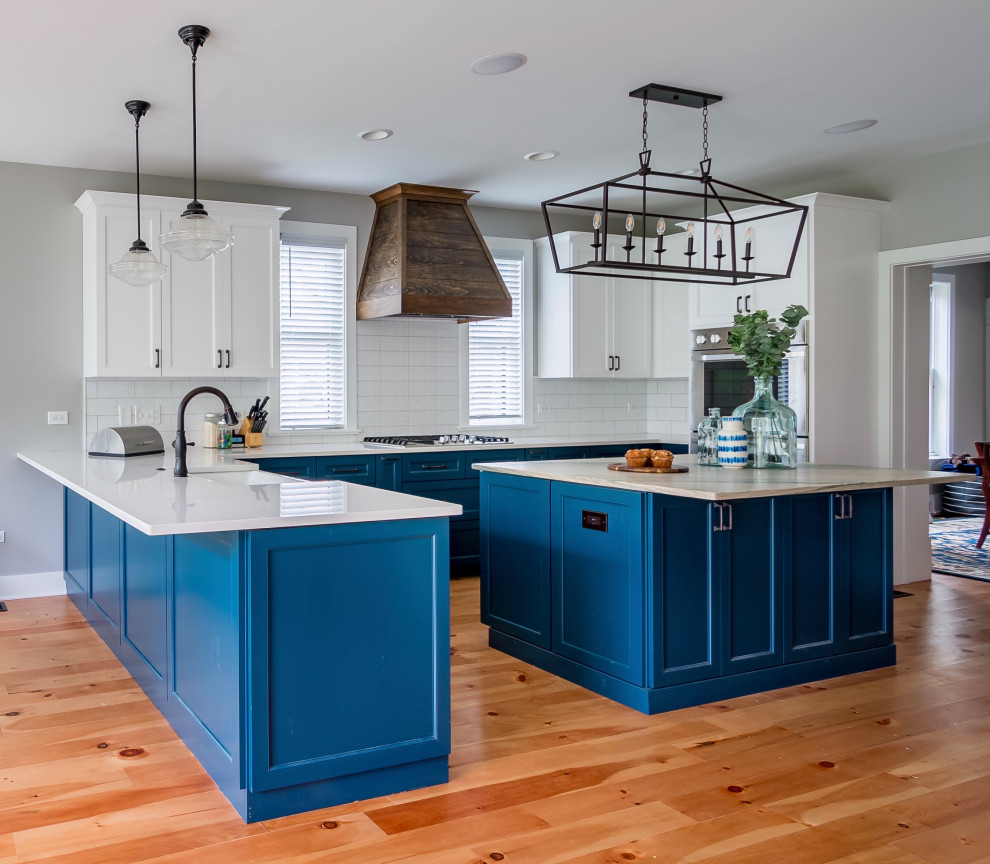 Inspiration for a mid-sized country l-shaped eat-in kitchen in Chicago with a farmhouse sink, recessed-panel cabinets, blue cabinets, quartzite benchtops, white splashback, ceramic splashback, stainless steel appliances, light hardwood floors, with island, multi-coloured floor and multi-coloured benchtop.