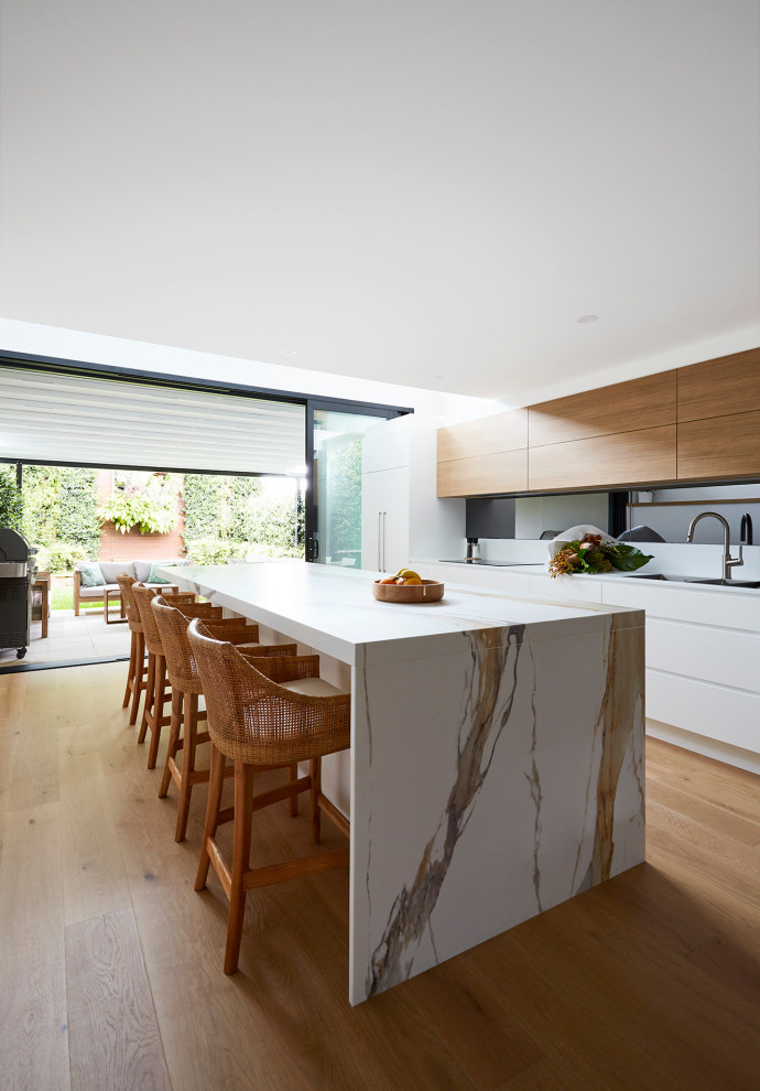 Photo of a large contemporary l-shaped kitchen pantry in Sydney with a double-bowl sink, flat-panel cabinets, white cabinets, quartz benchtops, multi-coloured splashback, mirror splashback, black appliances, laminate floors, with island and multi-coloured benchtop.