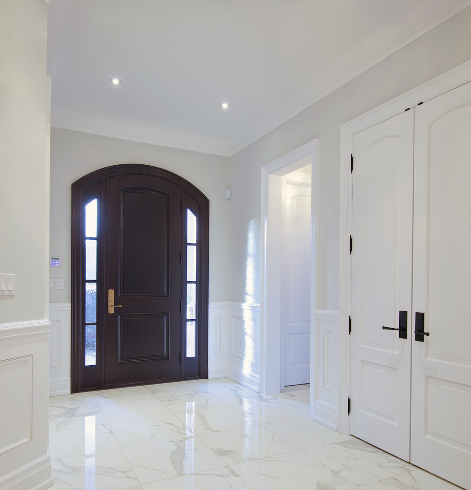 This is an example of a large contemporary front door in Toronto with white walls, marble floors, a single front door and a dark wood front door.