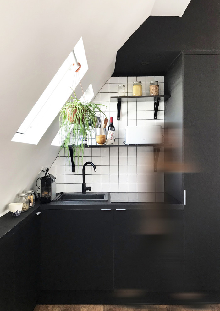 Small contemporary l-shaped open plan kitchen with a drop-in sink, beaded inset cabinets, black cabinets, laminate benchtops, white splashback, ceramic splashback, panelled appliances, laminate floors and black benchtop.