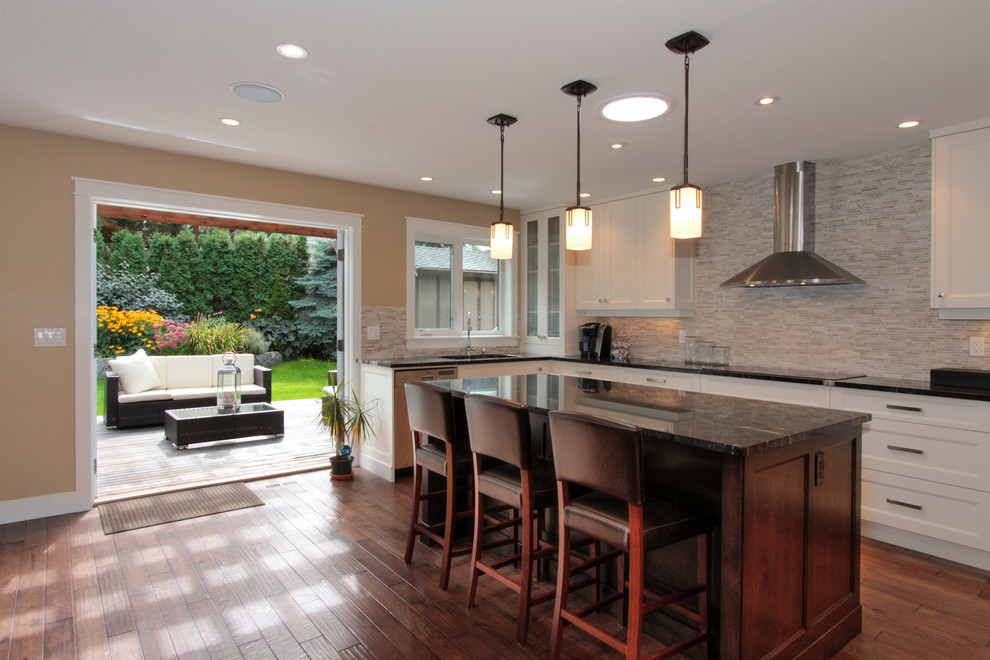 Mid-sized transitional u-shaped medium tone wood floor eat-in kitchen photo in Vancouver with an undermount sink, recessed-panel cabinets, white cabinets, granite countertops, beige backsplash, glass tile backsplash, stainless steel appliances and an island