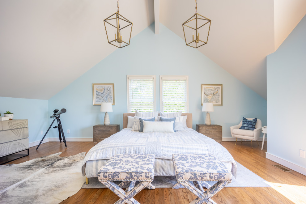Aménagement d'une grande chambre parentale bord de mer avec un mur bleu, un sol en bois brun et un plafond voûté.