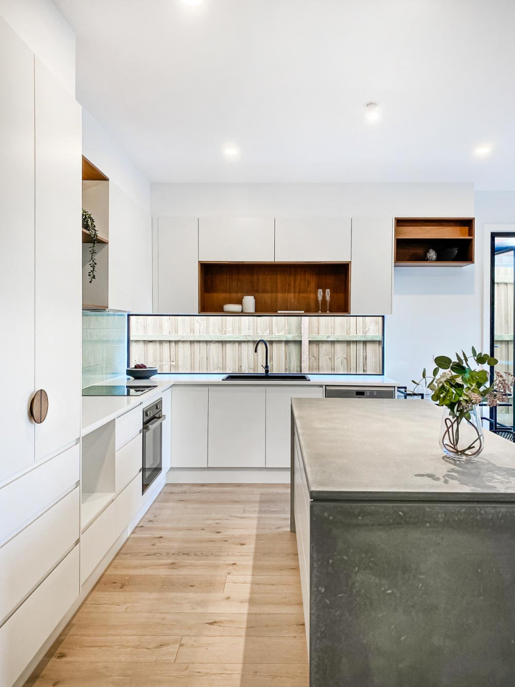Photo of a contemporary l-shaped kitchen in Melbourne with a drop-in sink, flat-panel cabinets, white cabinets, stainless steel appliances, light hardwood floors, with island, beige floor and grey benchtop.