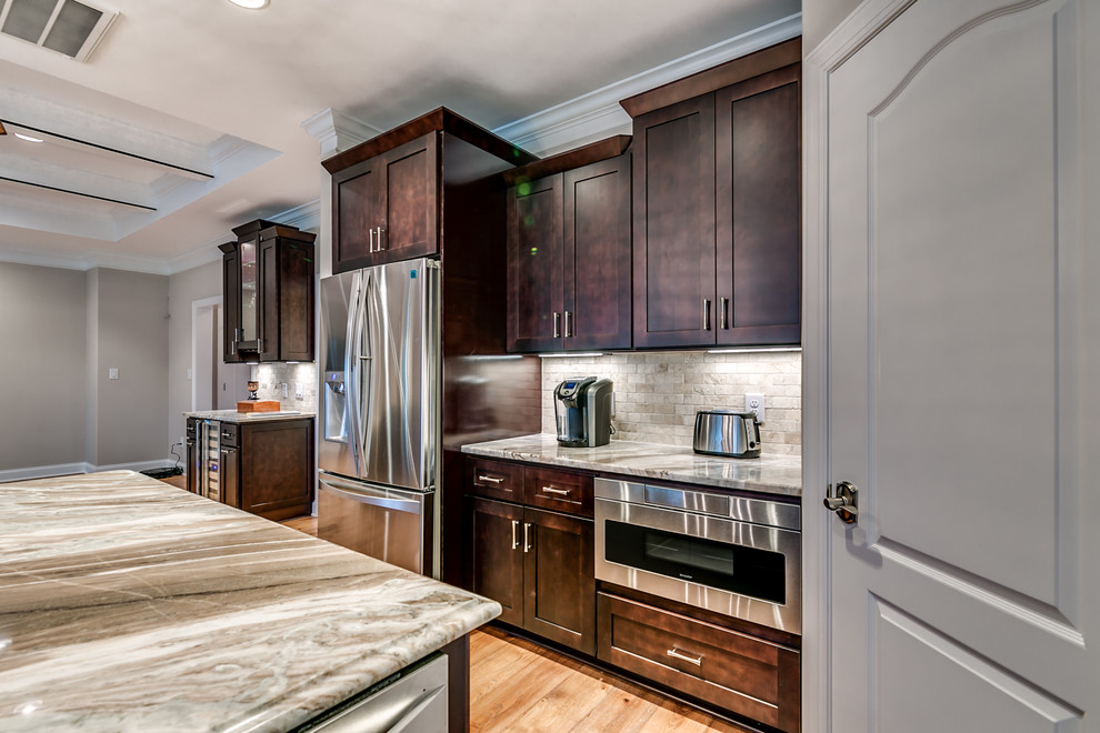 Example of a large transitional l-shaped medium tone wood floor and brown floor open concept kitchen design with an undermount sink, shaker cabinets, dark wood cabinets, granite countertops, gray backsplash, stone tile backsplash, stainless steel appliances, an island and gray countertops