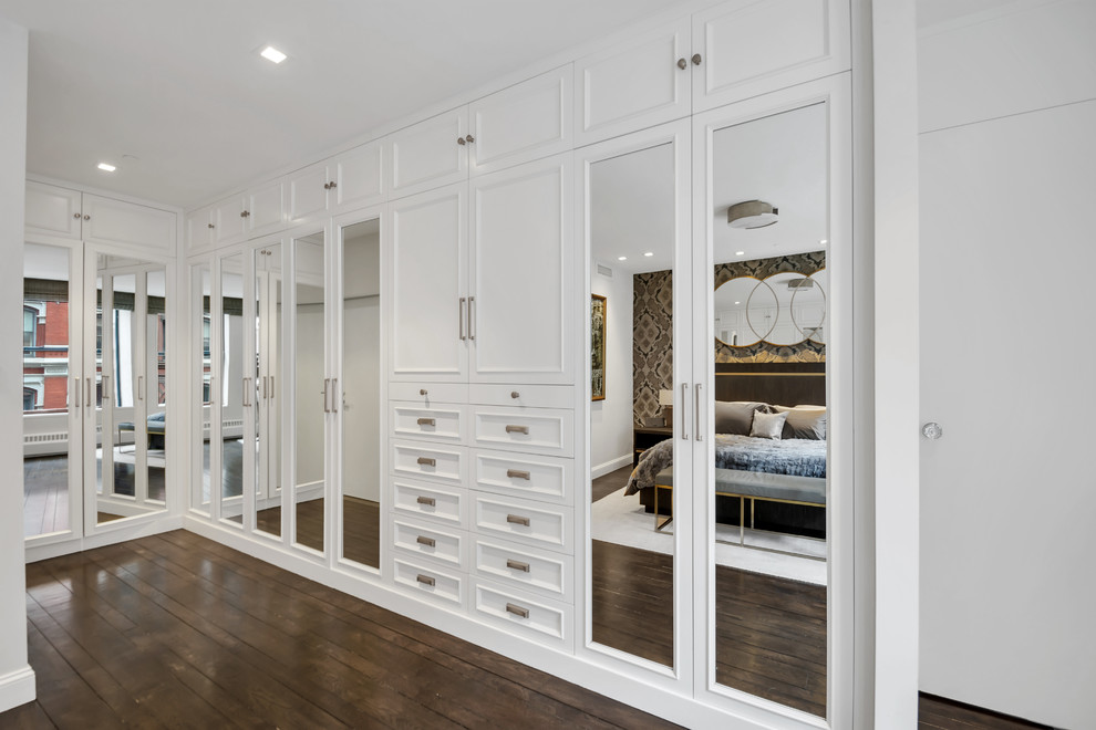 Photo of a large traditional gender-neutral built-in wardrobe in New York with raised-panel cabinets, white cabinets, dark hardwood floors and brown floor.