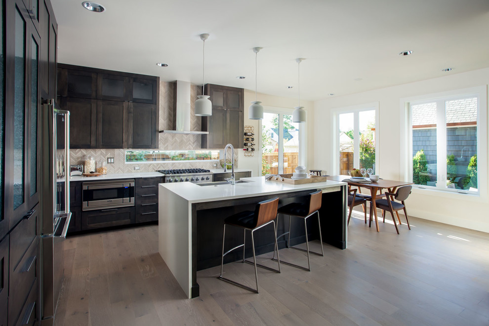 This is an example of a contemporary l-shaped kitchen in Portland with a farmhouse sink, shaker cabinets, dark wood cabinets, grey splashback, medium hardwood floors and with island.