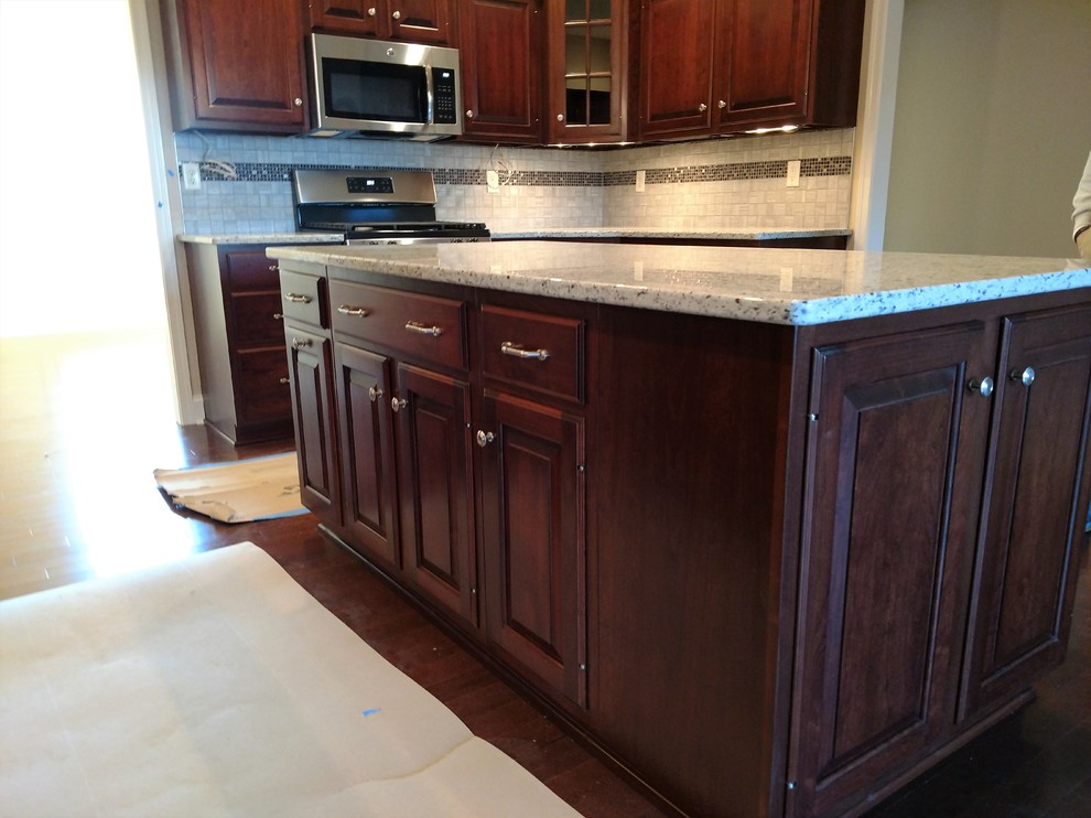 Example of a mid-sized transitional kitchen design with an undermount sink, raised-panel cabinets, dark wood cabinets, quartz countertops, multicolored backsplash, ceramic backsplash, stainless steel appliances and an island