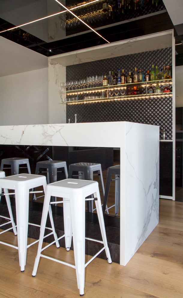Inspiration for a large modern galley seated home bar in Melbourne with flat-panel cabinets, a drop-in sink, black cabinets, tile benchtops, grey splashback, mosaic tile splashback, medium hardwood floors, brown floor and white benchtop.