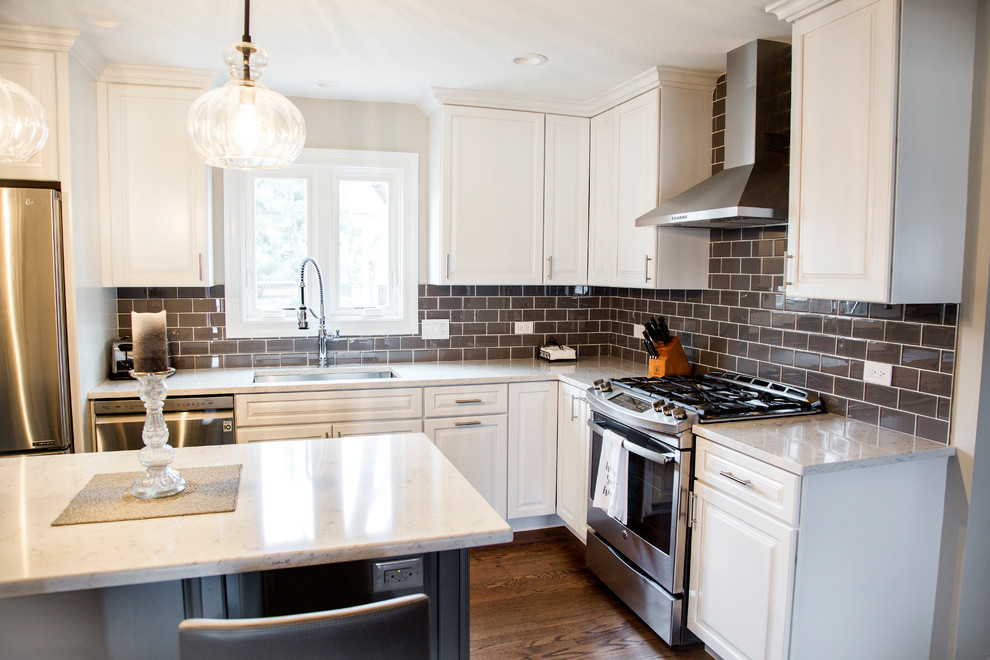 Example of a mid-sized transitional l-shaped medium tone wood floor and brown floor eat-in kitchen design in Chicago with an undermount sink, raised-panel cabinets, white cabinets, quartz countertops, gray backsplash, ceramic backsplash, stainless steel appliances, an island and white countertops