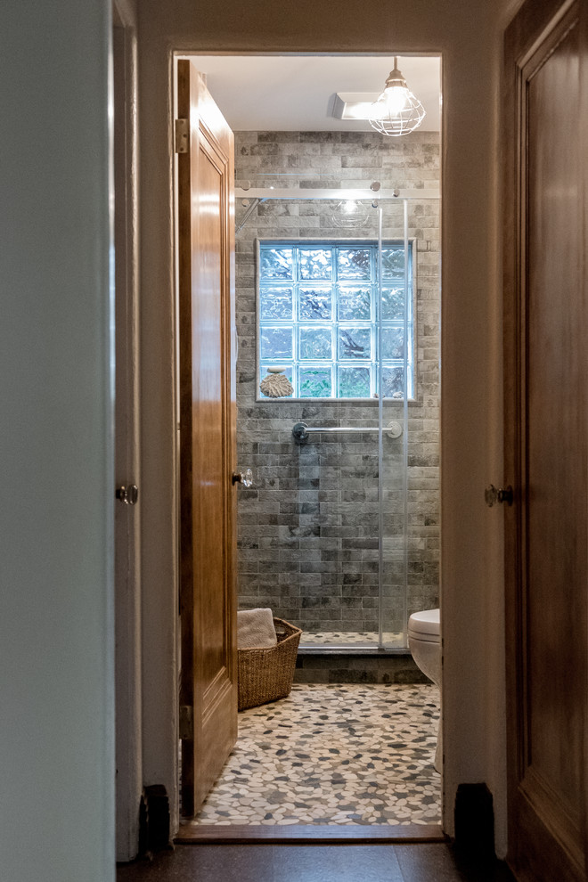 Mid-sized contemporary master bathroom in Providence with flat-panel cabinets, dark wood cabinets, a curbless shower, a two-piece toilet, gray tile, stone tile, grey walls, pebble tile floors, a wall-mount sink, multi-coloured floor, a hinged shower door and white benchtops.