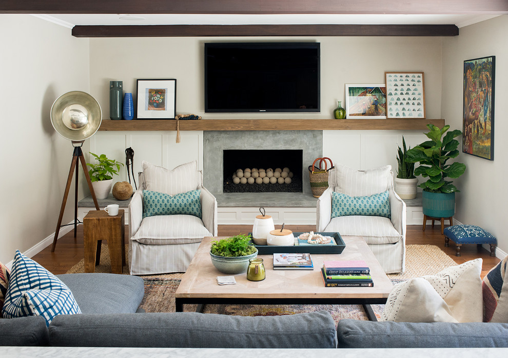 This is an example of an eclectic family room in Los Angeles with white walls, medium hardwood floors, a standard fireplace, a concrete fireplace surround, a wall-mounted tv and brown floor.