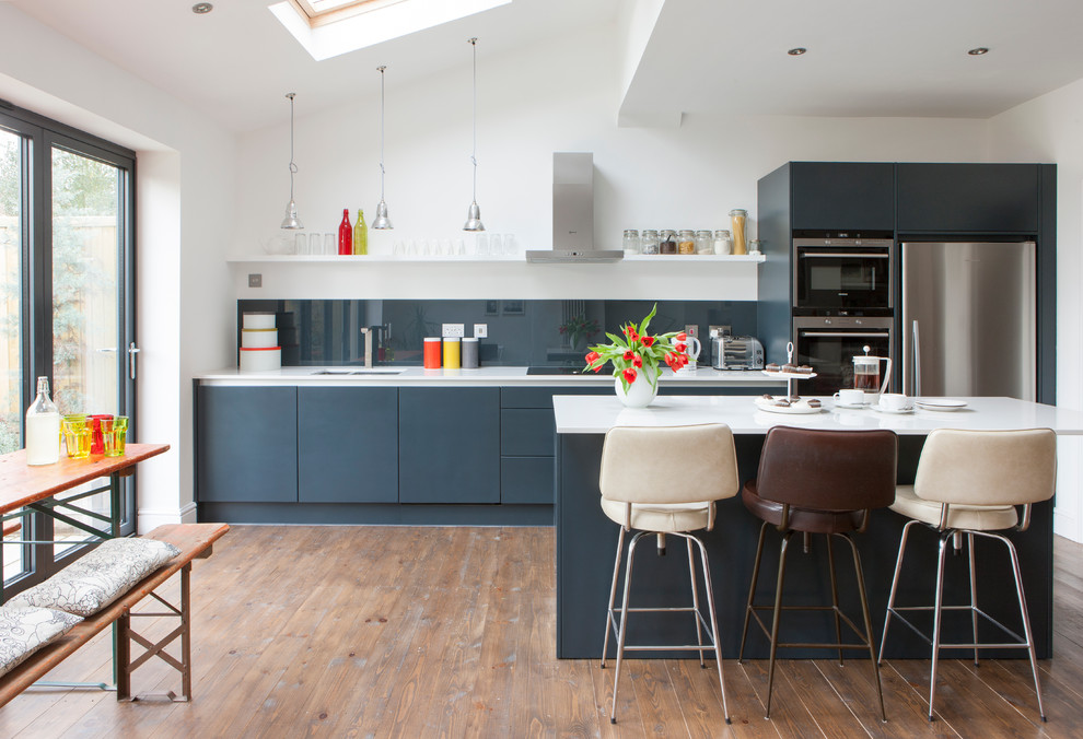 Design ideas for a medium sized contemporary single-wall kitchen/diner in London with flat-panel cabinets, grey cabinets, composite countertops, grey splashback, glass sheet splashback, an island, an integrated sink, integrated appliances, brown floors, white worktops and a drop ceiling.