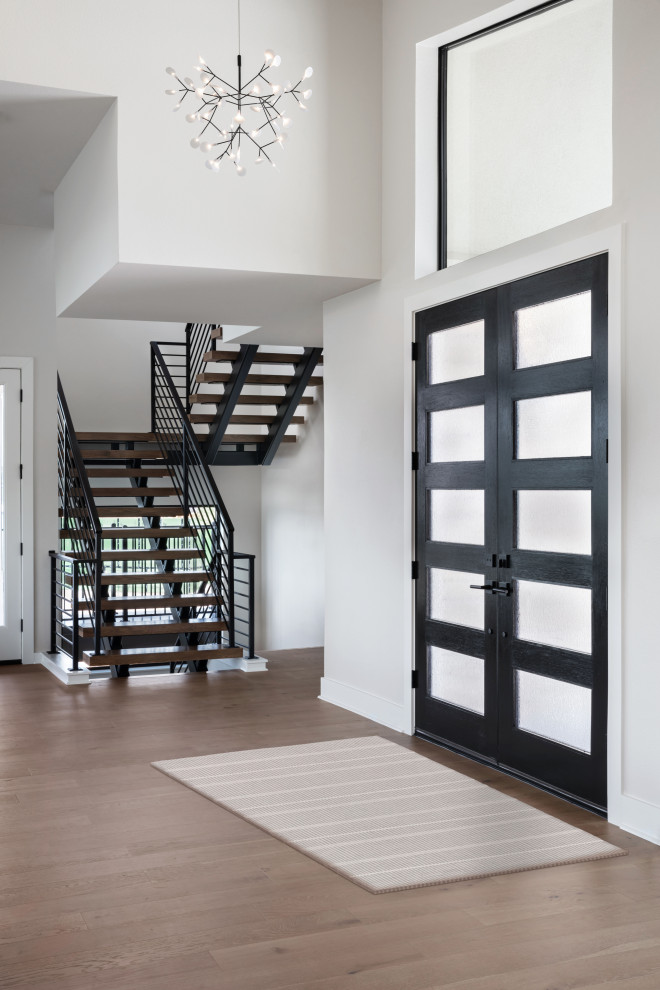 Imagen de puerta principal actual con paredes blancas, suelo de madera clara, puerta doble, puerta negra y suelo beige