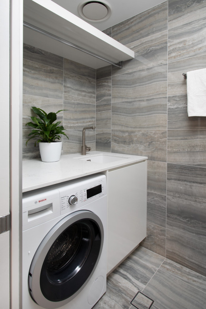 Inspiration for a small contemporary galley dedicated laundry room in Brisbane with white cabinets, grey walls, porcelain floors, grey floor and white benchtop.