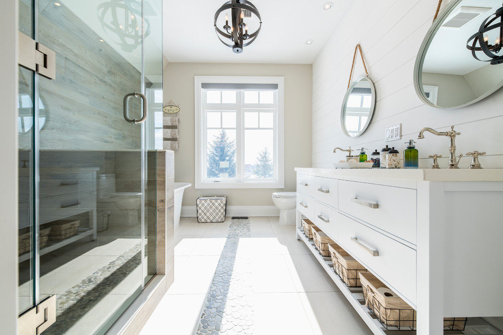 Design ideas for a mid-sized transitional kids bathroom in Toronto with furniture-like cabinets, distressed cabinets, a drop-in tub, an alcove shower, a two-piece toilet, beige tile, ceramic tile, beige walls, pebble tile floors, a drop-in sink, beige floor and a hinged shower door.