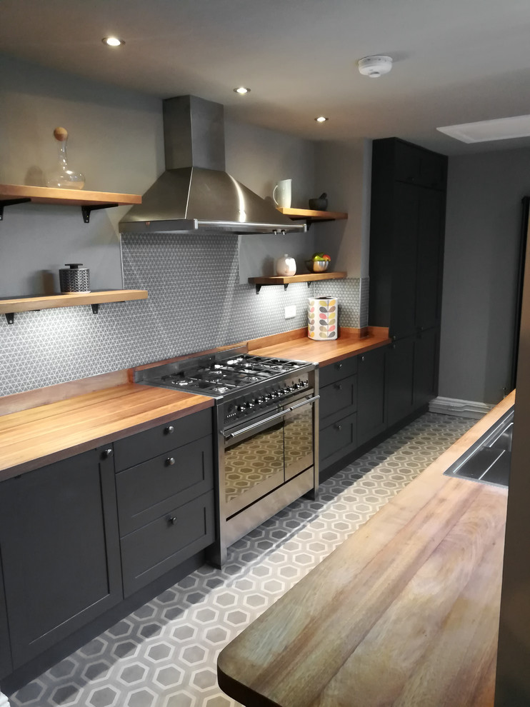 Mid-sized contemporary galley separate kitchen in Other with a double-bowl sink, shaker cabinets, grey cabinets, wood benchtops, grey splashback, mosaic tile splashback, stainless steel appliances, vinyl floors, no island, grey floor and brown benchtop.