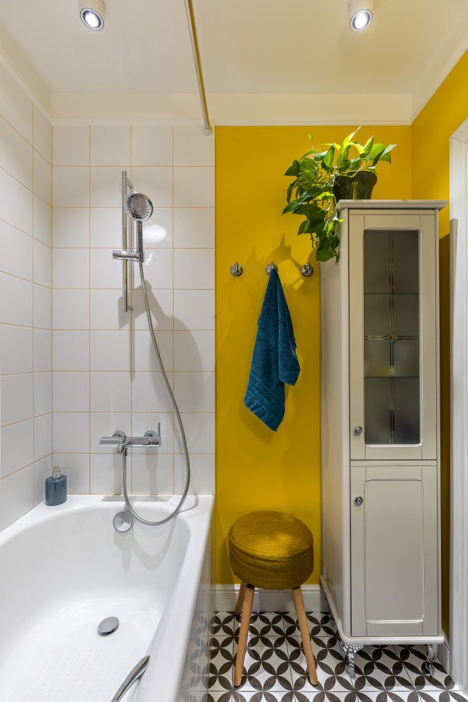Inredning av ett modernt litet vit vitt badrum, med luckor med profilerade fronter, blå skåp, ett undermonterat badkar, en dusch/badkar-kombination, vit kakel, keramikplattor, gula väggar, klinkergolv i keramik, ett fristående handfat, bänkskiva i akrylsten och svart golv