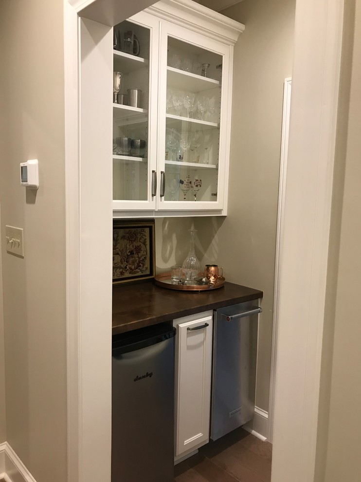 This is an example of a small traditional single-wall wet bar in Other with no sink, glass-front cabinets, white cabinets, copper benchtops, dark hardwood floors, brown floor and brown benchtop.