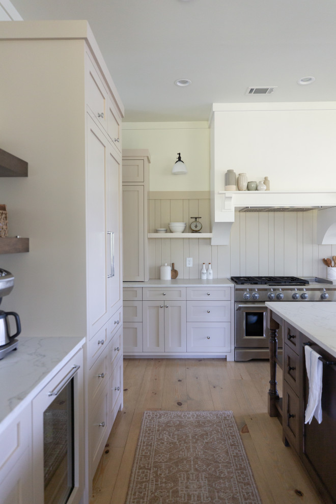 Photo of a country kitchen in Atlanta with shaker cabinets, beige cabinets, quartz benchtops, beige splashback, shiplap splashback, stainless steel appliances, light hardwood floors and with island.