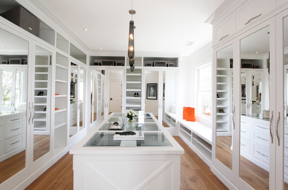 Design ideas for a large modern gender-neutral dressing room in New York with glass-front cabinets, white cabinets and light hardwood floors.