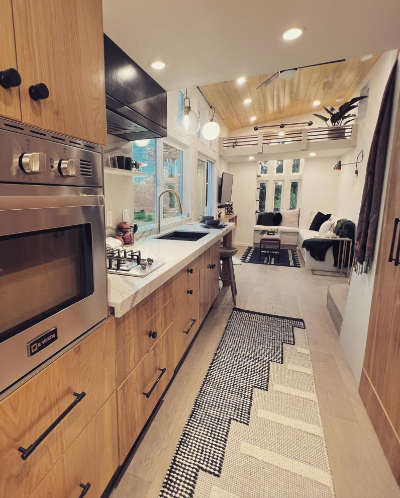 This is an example of a mid-sized contemporary galley open plan kitchen in Hawaii with an undermount sink, flat-panel cabinets, medium wood cabinets, granite benchtops, white splashback, granite splashback, stainless steel appliances, light hardwood floors, no island, beige floor, white benchtop and timber.