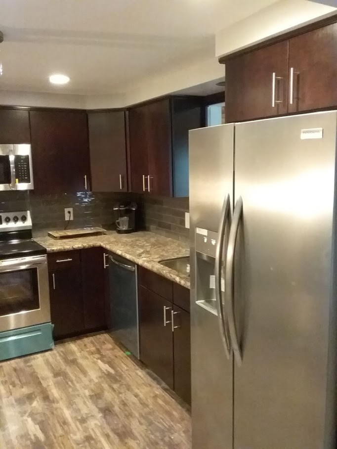 Photo of a mid-sized l-shaped separate kitchen in New York with an undermount sink, flat-panel cabinets, dark wood cabinets, laminate benchtops, beige splashback, ceramic splashback, stainless steel appliances, vinyl floors, no island, brown floor and brown benchtop.