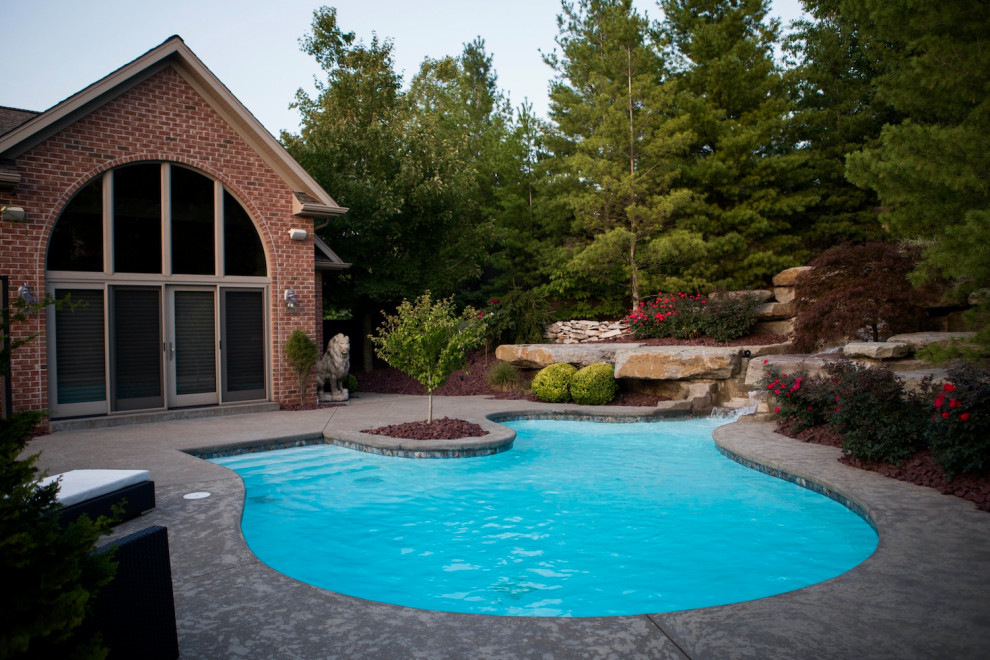 Exempel på en stor klassisk anpassad pool på baksidan av huset, med stämplad betong