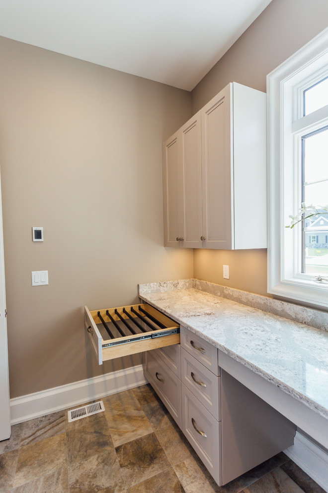 Photo of a large transitional u-shaped dedicated laundry room in New York with recessed-panel cabinets, beige cabinets, solid surface benchtops, beige walls, travertine floors and a side-by-side washer and dryer.