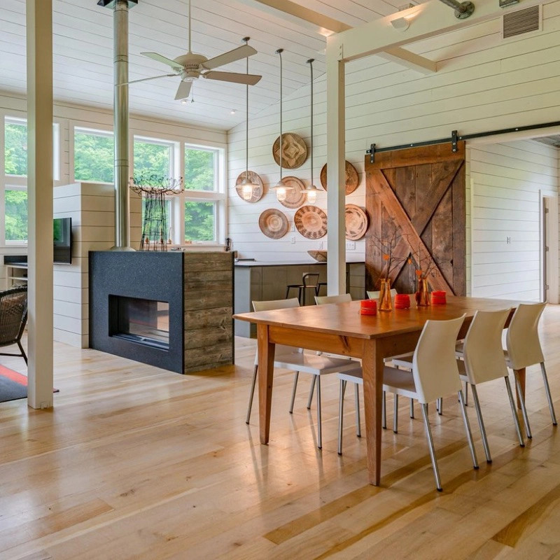 This is an example of a country kitchen/dining combo in Other with light hardwood floors, a two-sided fireplace and timber.