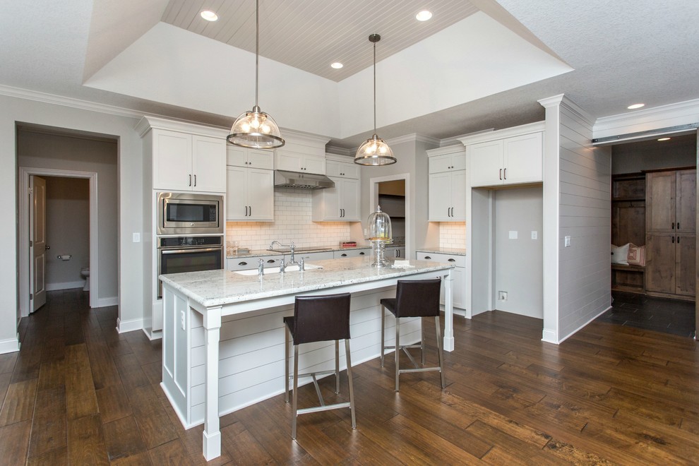 Example of a mid-sized transitional single-wall medium tone wood floor and beige floor open concept kitchen design with a farmhouse sink, recessed-panel cabinets, white cabinets, granite countertops, white backsplash, stainless steel appliances, an island and ceramic backsplash