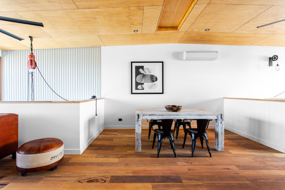 Photo of an industrial dining room in Adelaide with white walls, medium hardwood floors, brown floor, vaulted and wood.
