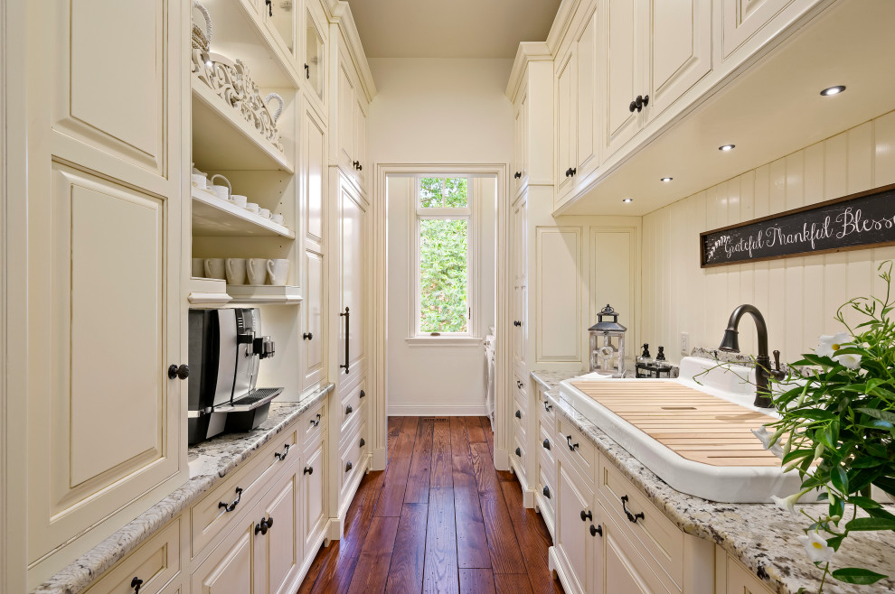 Inspiration for an expansive mediterranean l-shaped kitchen pantry in Kansas City with a farmhouse sink, glass-front cabinets, white cabinets, granite benchtops, beige splashback, stainless steel appliances, medium hardwood floors, with island, brown floor and brown benchtop.