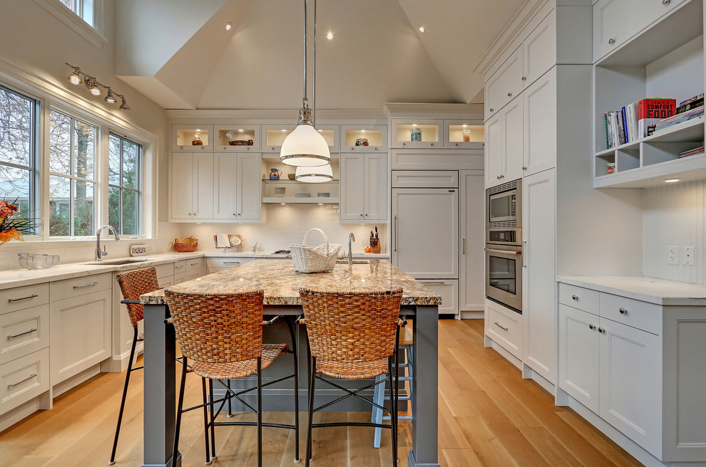 Inspiration for a transitional l-shaped light wood floor eat-in kitchen remodel in Toronto with an undermount sink, white cabinets, white backsplash, stainless steel appliances, an island and recessed-panel cabinets