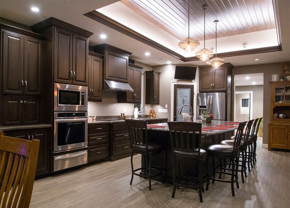 Large traditional l-shaped eat-in kitchen in Other with an integrated sink, raised-panel cabinets, dark wood cabinets, granite benchtops, stainless steel appliances, vinyl floors and with island.