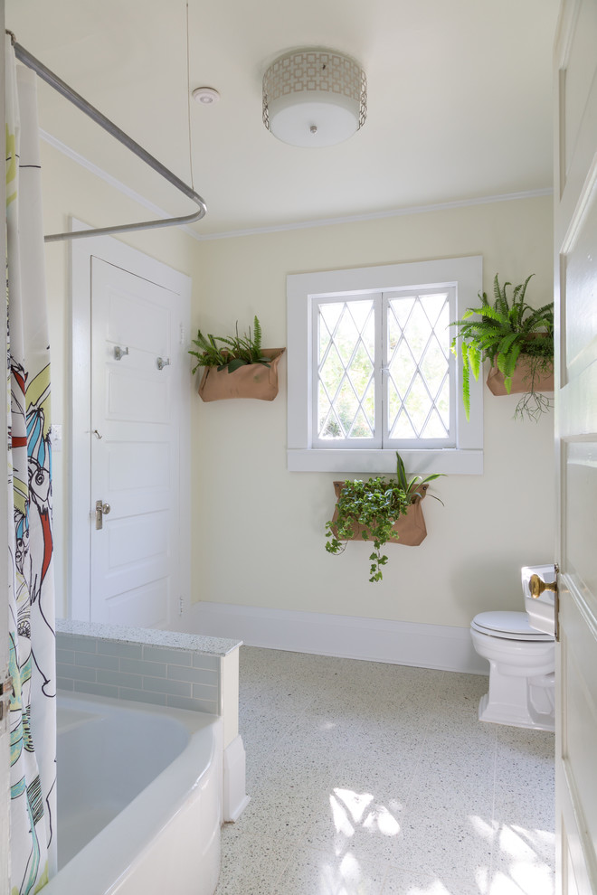 Small arts and crafts kids bathroom in New Orleans with glass-front cabinets, a one-piece toilet, white cabinets, a freestanding tub, a shower/bathtub combo, gray tile, subway tile, beige walls, ceramic floors and a pedestal sink.