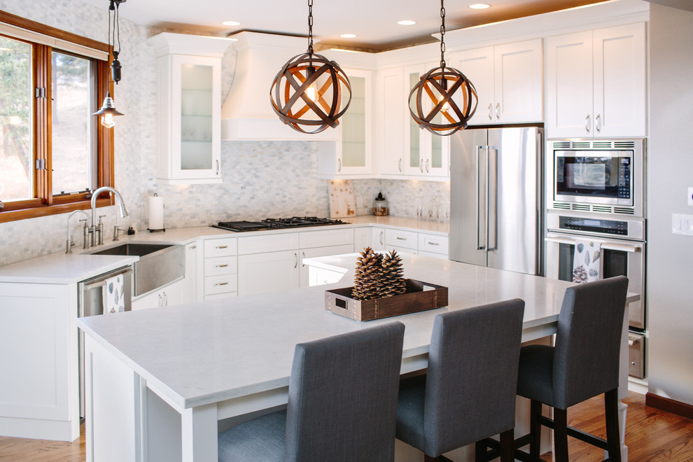Design ideas for a mid-sized transitional u-shaped eat-in kitchen in Denver with a farmhouse sink, shaker cabinets, white cabinets, quartz benchtops, white splashback, stone tile splashback, stainless steel appliances, medium hardwood floors, with island and brown floor.