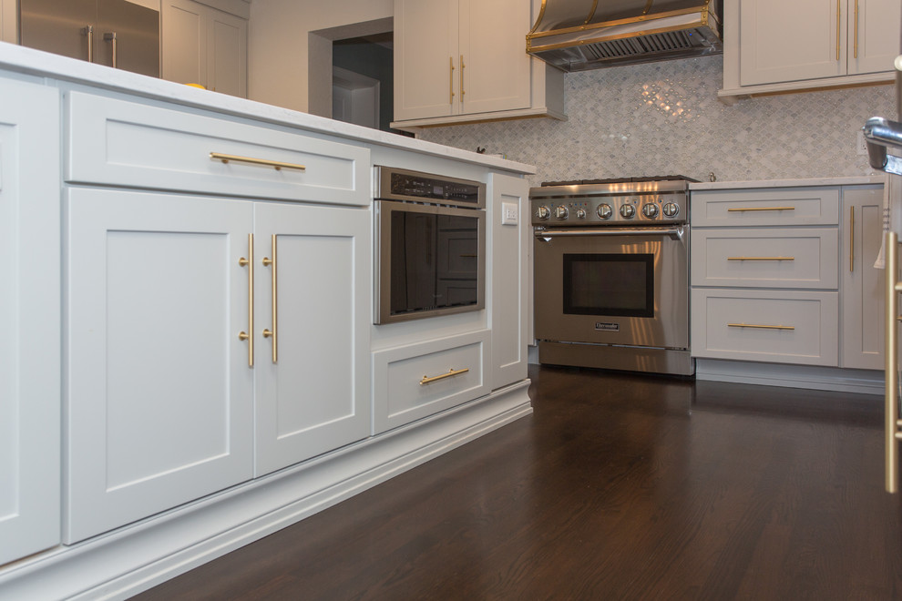 This is an example of a mid-sized transitional l-shaped open plan kitchen in Tampa with a farmhouse sink, shaker cabinets, grey cabinets, quartz benchtops, multi-coloured splashback, glass tile splashback, stainless steel appliances, dark hardwood floors, with island and brown floor.