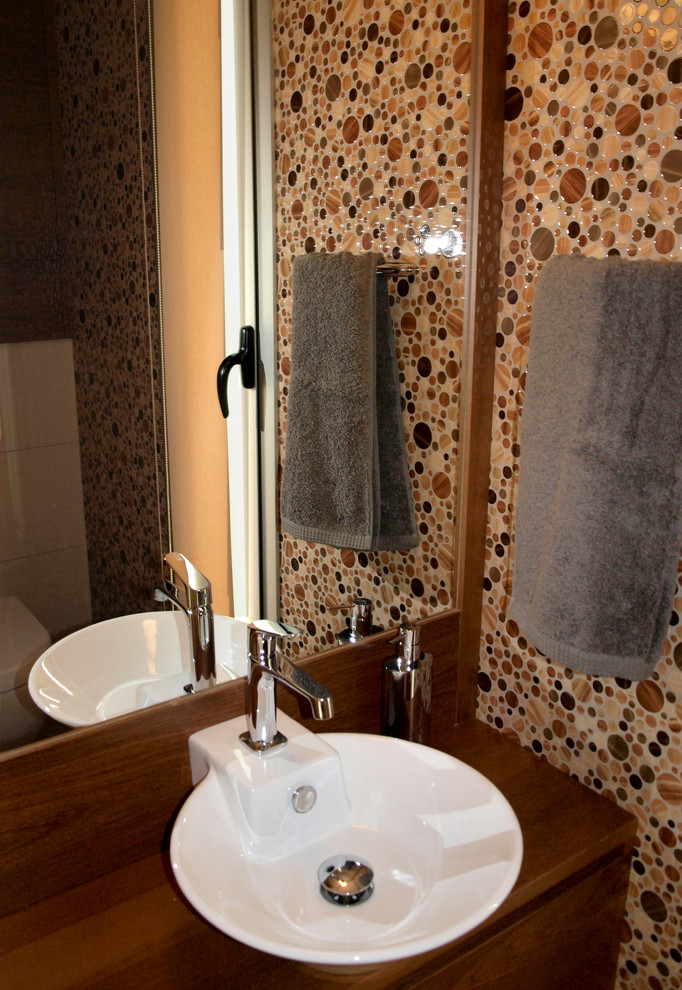 Photo of a small modern powder room in Barcelona with furniture-like cabinets, dark wood cabinets, a wall-mount toilet, multi-coloured tile, ceramic tile, multi-coloured walls, porcelain floors, a vessel sink and wood benchtops.