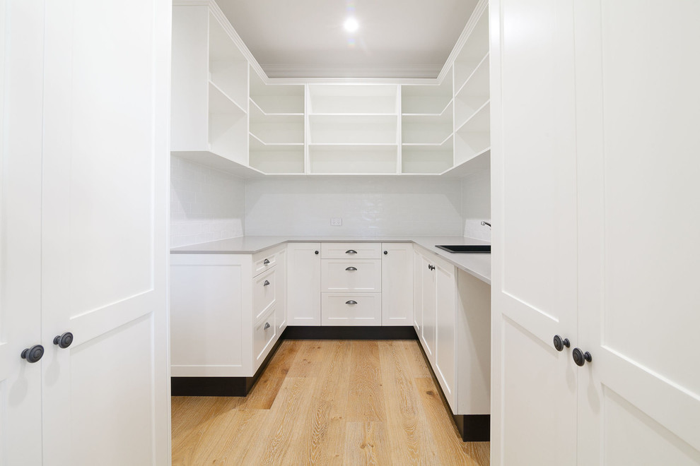 Inspiration for a mid-sized traditional u-shaped kitchen pantry in Brisbane with a drop-in sink, shaker cabinets, white cabinets, quartz benchtops, white splashback, porcelain splashback and grey benchtop.