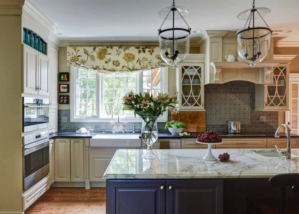 Example of a large classic u-shaped medium tone wood floor open concept kitchen design in Chicago with a farmhouse sink, white cabinets, gray backsplash, paneled appliances, an island, subway tile backsplash and granite countertops
