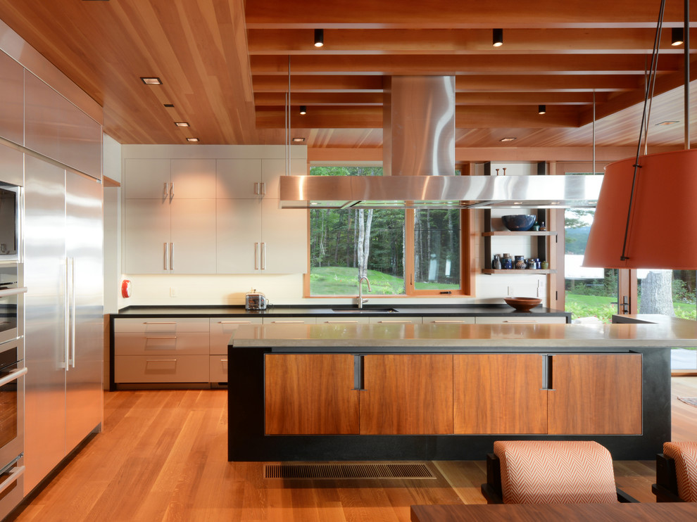Contemporary open plan kitchen in Other with an undermount sink, flat-panel cabinets, grey cabinets, stainless steel appliances, medium hardwood floors, with island, brown floor and black benchtop.