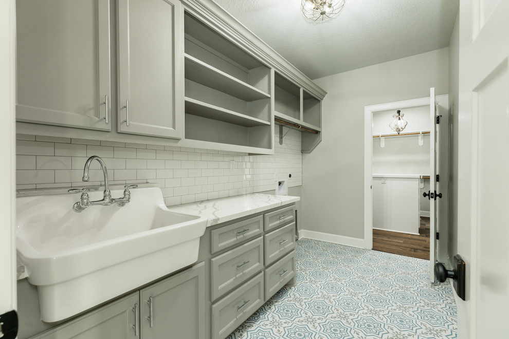 This is an example of a large country single-wall utility room in Houston with a farmhouse sink, recessed-panel cabinets, grey cabinets, granite benchtops, grey walls, porcelain floors, a side-by-side washer and dryer, blue floor and white benchtop.
