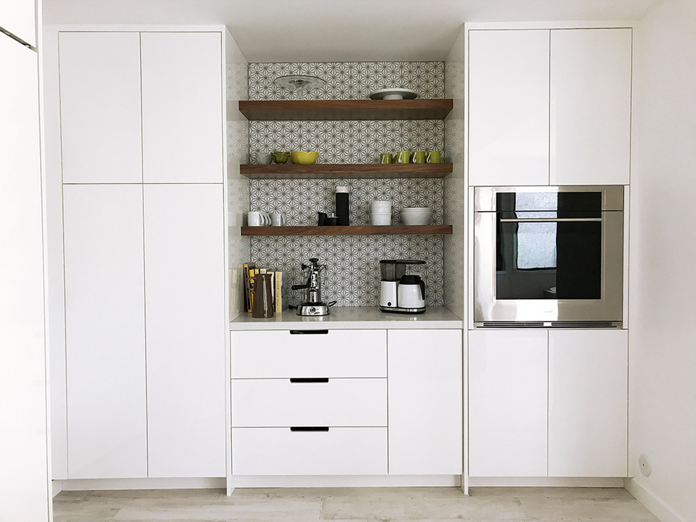 Photo of a small contemporary single-wall wet bar in Los Angeles with no sink, flat-panel cabinets, white cabinets, solid surface benchtops, grey splashback, ceramic splashback, light hardwood floors, beige floor and white benchtop.