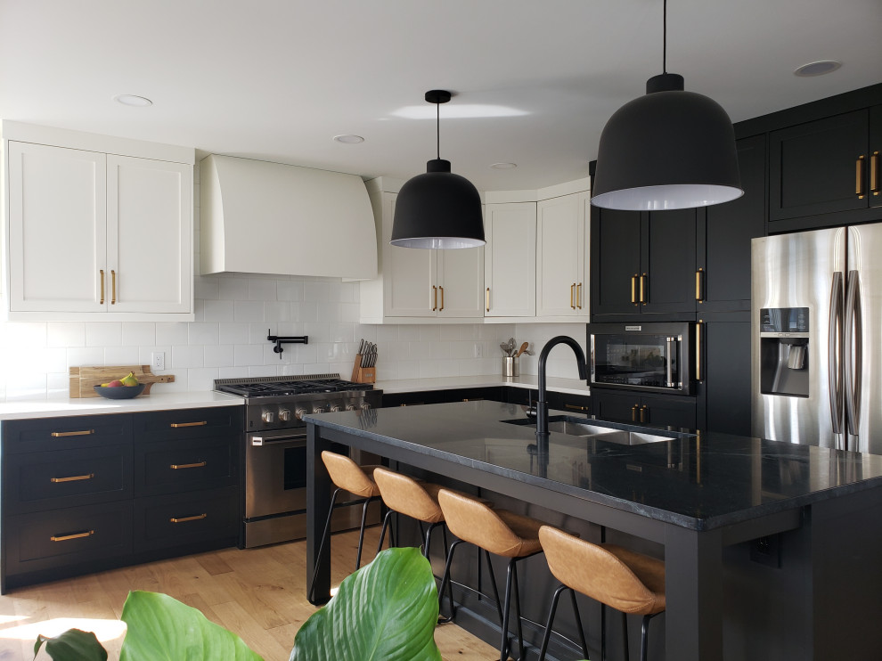 Inspiration for a large transitional l-shaped eat-in kitchen in Edmonton with an undermount sink, shaker cabinets, black cabinets, soapstone benchtops, white splashback, subway tile splashback, stainless steel appliances, light hardwood floors, with island, black benchtop and brown floor.