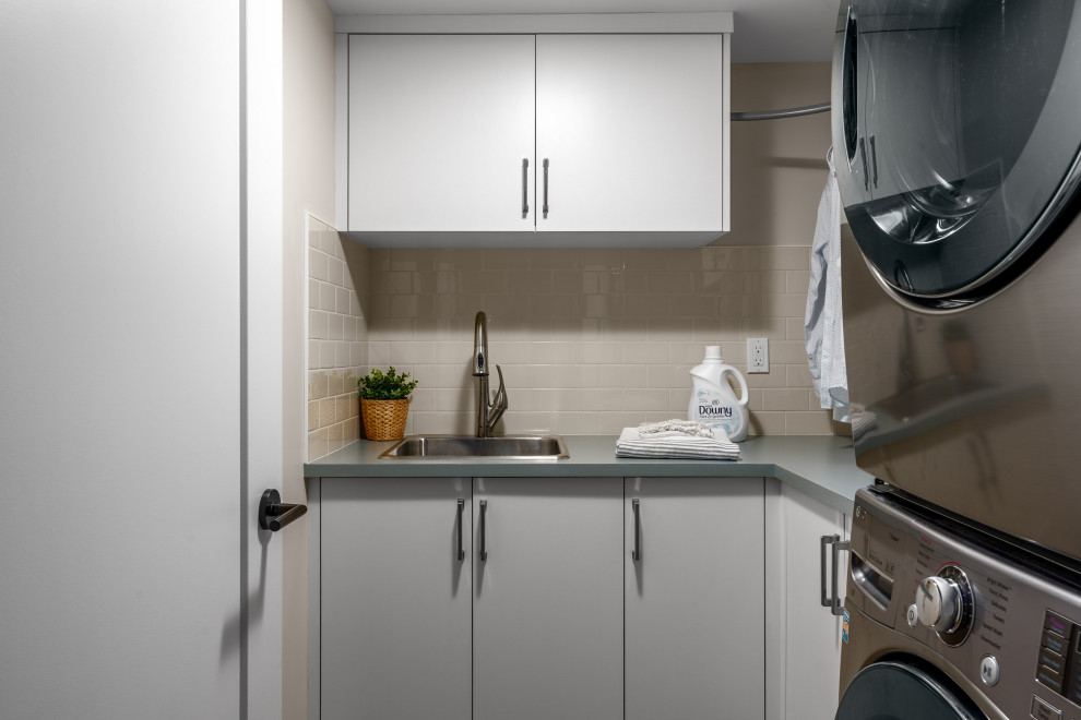 This is an example of a small l-shaped dedicated laundry room in Vancouver with a drop-in sink, flat-panel cabinets, white cabinets, laminate benchtops, white walls, a stacked washer and dryer and blue benchtop.