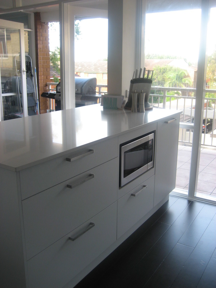 Photo of a small modern l-shaped kitchen in Sydney with a single-bowl sink, flat-panel cabinets, white cabinets, quartz benchtops, white splashback, stainless steel appliances and with island.